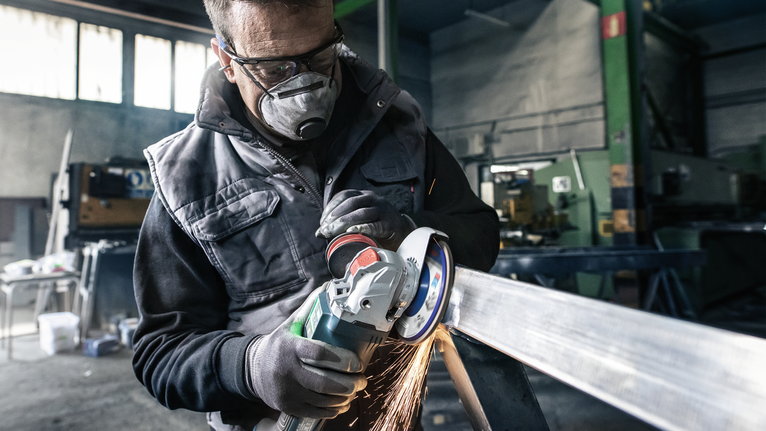 PRO X571 Flap Disc, Straight, 125 mm, G40, X-Lock Person wearing safety equipment grinds a metal beam, producing sparks.