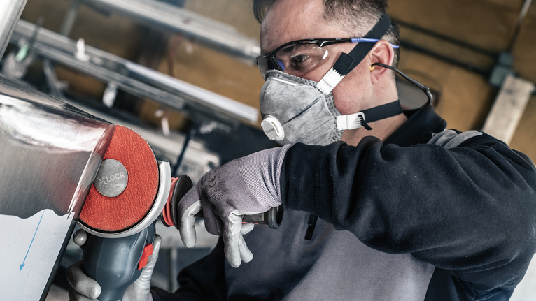 PRO R780 X-Lock Fibre Disc, 125 mm, G36 Person wearing safety equipment polishes metal with a power tool.