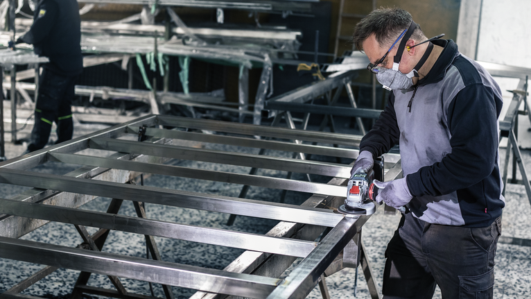 PRO R780 X-Lock Fibre Disc, 125 mm, G36 A person wearing safety equipment grinds a metal frame in a workshop.