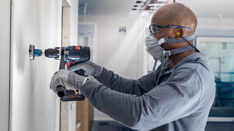 PRO Multi Material PC Plus Hole Saw, 51 mm Person wearing safety equipment drills a circular hole into an interior wall.