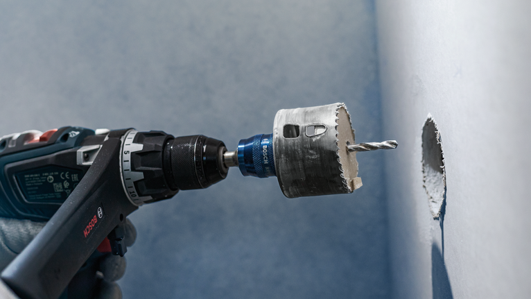 PRO Multi Material PC Plus Hole Saw, 51 mm Person wearing safety equipment drills a circular hole into a wall.