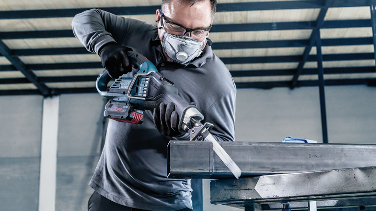Person wearing safety equipment uses a reciprocating saw to cut a metal beam.