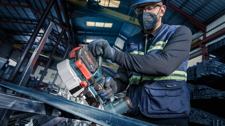 PRO CB281418 Band Saw Blade, 733 mm, 2 pcs Person wearing safety equipment cuts metal with a portable power saw in an industrial setting.