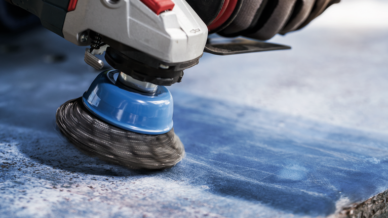PRO Metal heavy Cup Brush, 75 x 0.5 mm, Thread Person wearing safety equipment grinds a blue stone surface with a wire cup brush.