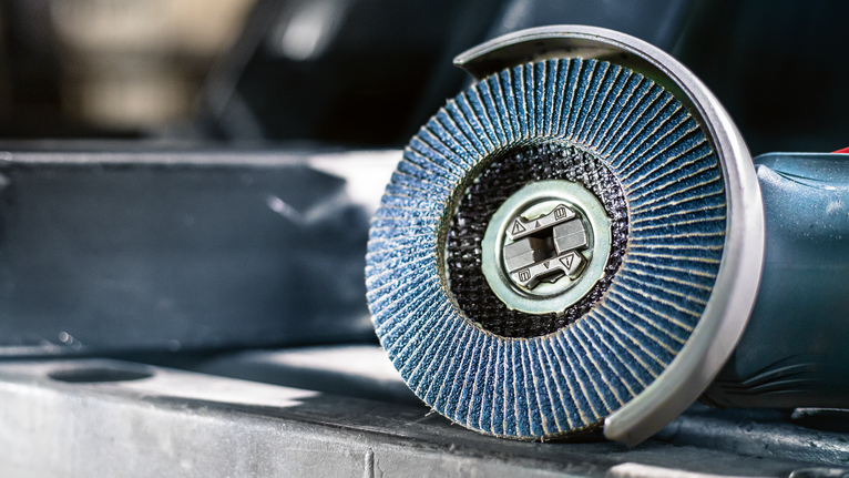 PRO X571 Flap Disc, Angled, 125 mm, G40, X-Lock A close-up of a blue flap disc grinder resting on a metal surface.