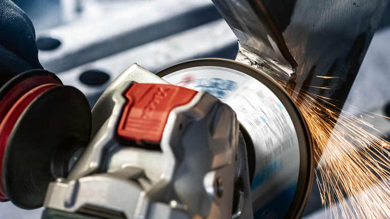 PRO X571 Flap Disc, Angled, 125 mm, G40, X-Lock A person wearing safety equipment grinds metal, producing sparks with an angle grinder.