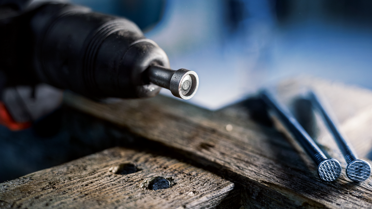 PRO SDS plus Rod Driver, 58 mm Power tool driving a fastener into wood next to several large nails.
