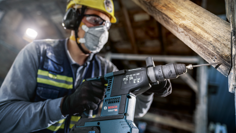 PRO SDS plus Rod Driver, 58 mm A person wearing safety equipment drills into a wooden beam with a power tool.