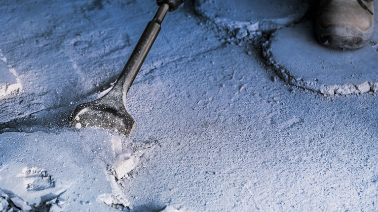 Person wearing safety equipment chisels a concrete surface.