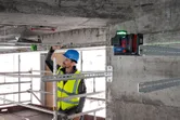 A person wearing safety equipment aligns metal bars using a laser leveling tool.