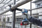 A person wearing safety equipment uses a cordless impact wrench on scaffolding.