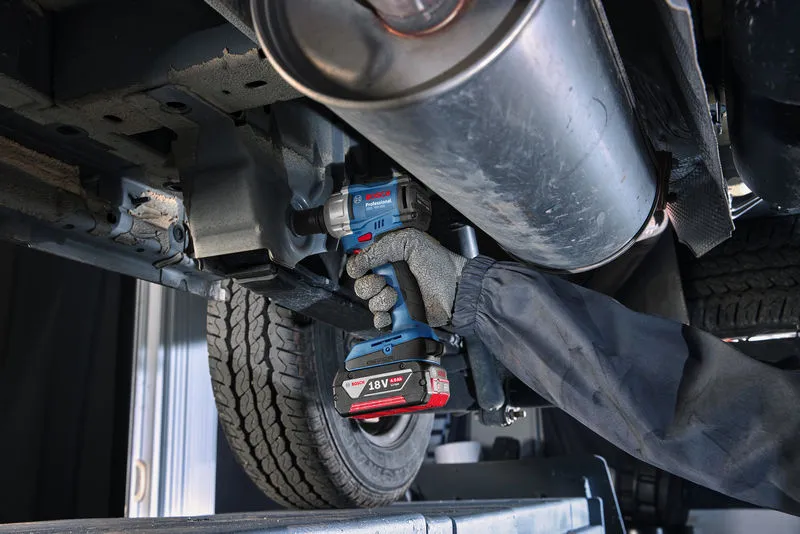 A person wearing safety equipment tightens a bolt on a car undercarriage with a cordless impact wrench.