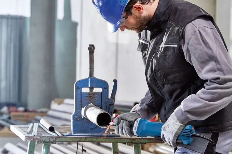 A person wearing safety equipment uses a straight grinder to work on a metal pipe.