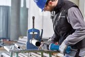 A person wearing safety equipment uses a straight grinder to work on a metal pipe.