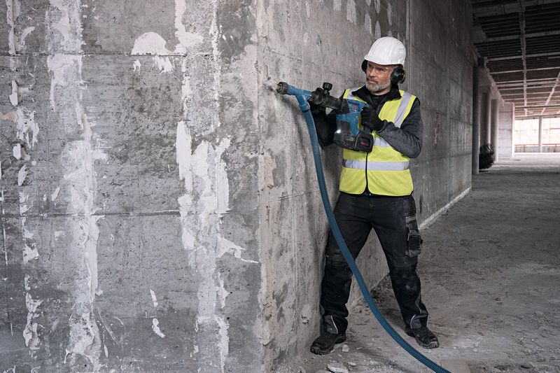 A person wearing safety equipment drills into a concrete wall with a power tool.