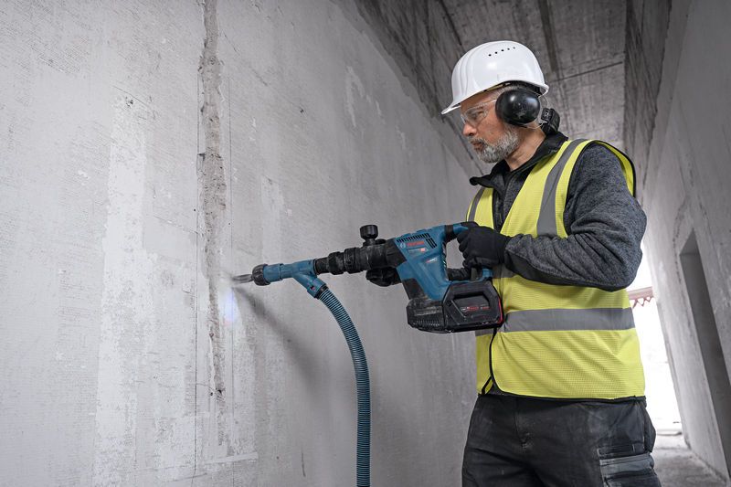 A person wearing safety equipment drills into a concrete wall with a power tool.