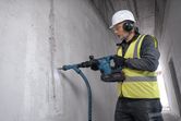 A person wearing safety equipment drills into a concrete wall with a power tool.