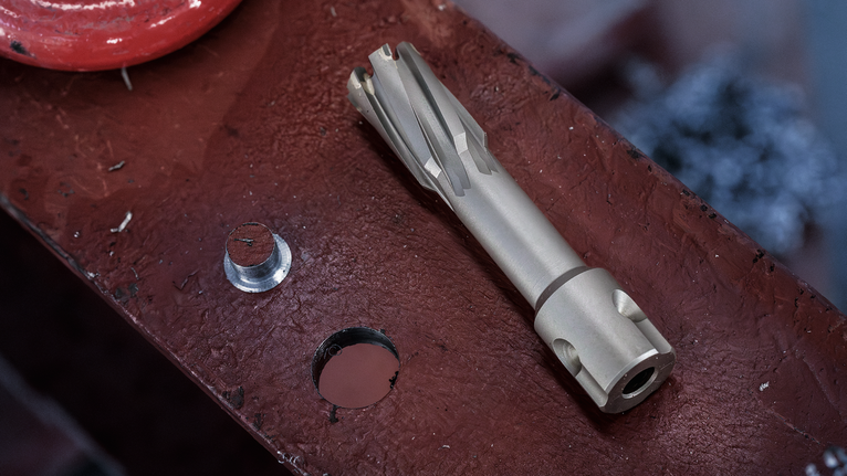 Annular cutter and drilled hole on a metal beam surface.