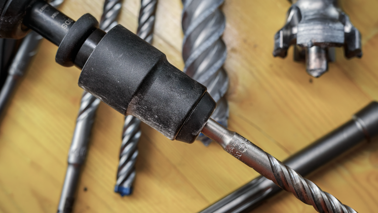 PRO Hammer Adapter, SDS max to SDS plus Close-up of various metal drill bits and a drill chuck on a wooden surface.