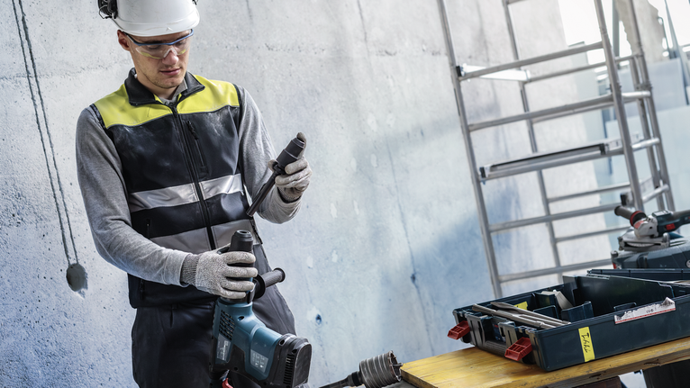 PRO Hammer Adapter, SDS max to SDS plus A person wearing safety equipment prepares a power tool on a worksite.
