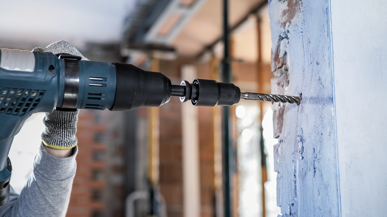 PRO Hammer Adapter, SDS max to SDS plus Person wearing safety equipment drills into a concrete wall with a power tool.
