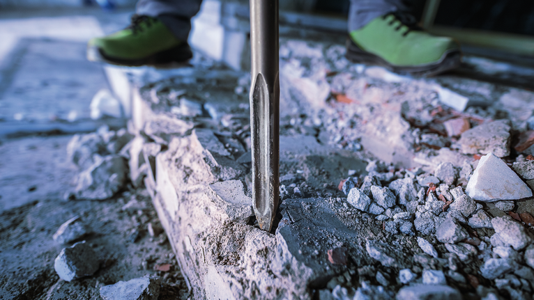 PRO HEX-5C Pointed Chisel 30 mm, 30 x 400 mm Person wearing safety equipment uses a demolition tool to break concrete.