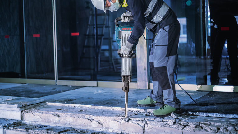 PRO HEX-5C Pointed Chisel 30 mm, 30 x 400 mm A person wearing safety equipment uses a demolition hammer to break concrete.