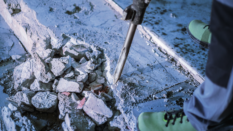 PRO HEX-5C Pointed Chisel 30 mm, 30 x 400 mm Person wearing safety equipment uses a demolition tool to break concrete flooring.
