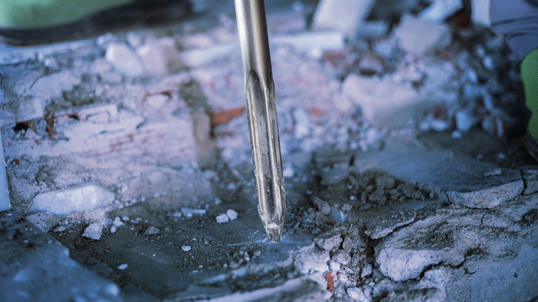 PRO HEX-5C Pointed Chisel 30 mm, 30 x 400 mm Person wearing safety equipment uses a demolition tool to break concrete.