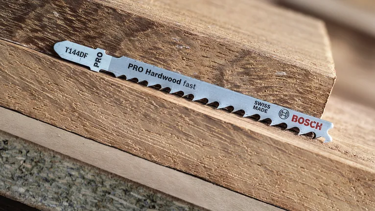 Jigsaw blade lying on stacked pieces of hardwood.