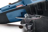 Person wearing safety equipment uses a wrench to adjust a chainsaw.