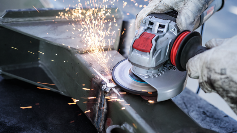 PRO Metal Bonded Grinding Disc, 125 x 6 x 22.23 mm, X-Lock Person wearing safety equipment grinds metal, creating sparks.