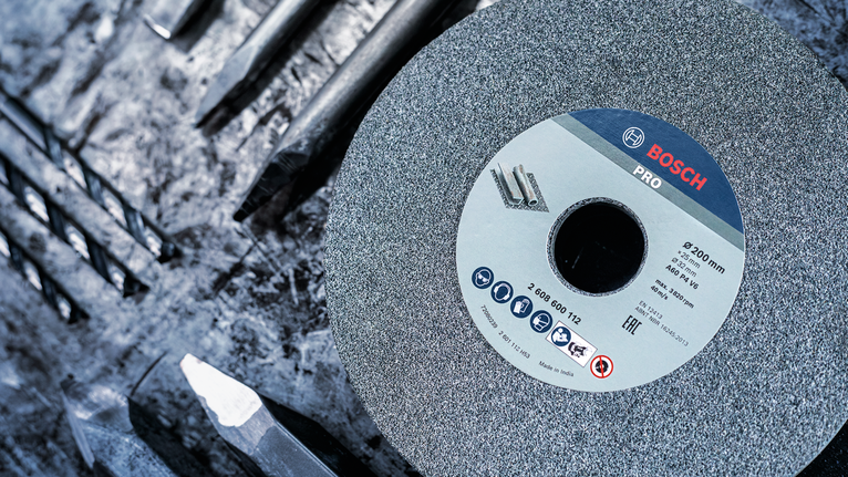 PRO Metal Grinding Wheel, 200 x 25 x 32 mm, G60 Large grinding wheel placed among several metal drill bits on a rough work surface.