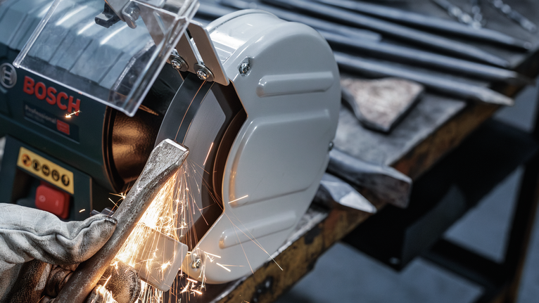 PRO Metal Grinding Wheel, 200 x 25 x 32 mm, G60 Person wearing safety equipment sharpens a metal tool on a bench grinder.