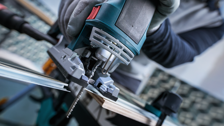 Person wearing safety equipment cuts wood with a jigsaw.