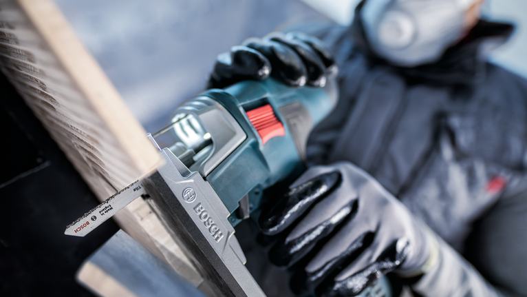 PRO Soft Tile T130RF Jigsaw Blade, 83 mm, 3 pcs Person wearing safety equipment uses a reciprocating saw to cut a wooden board.
