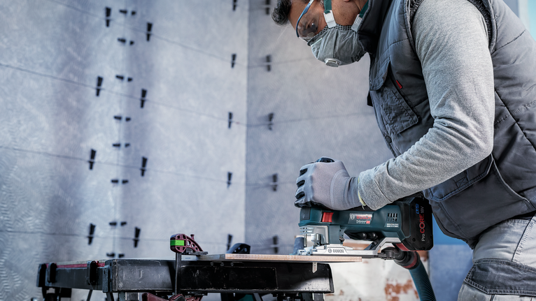 PRO Soft Tile T130RF Jigsaw Blade, 83 mm, 3 pcs A person wearing safety equipment uses a power saw to cut wood on a workbench.