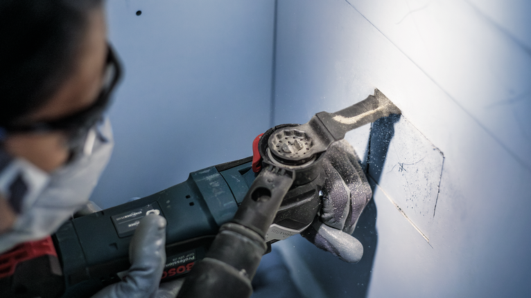 PRO AIZ 32 APIB Plunge Cut Blade, 32 x 50 mm Person wearing safety equipment uses a power tool to cut a square opening in a wall.