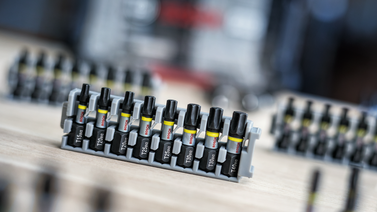 A set of screwdriver bits organized in a plastic holder on a wooden surface.