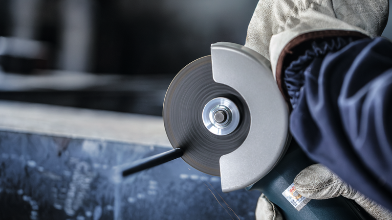 Person wearing safety equipment uses an angle grinder to cut metal.