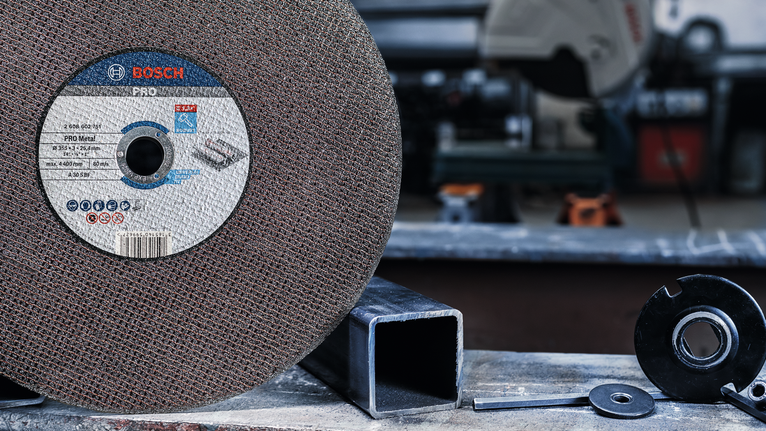 Large abrasive cutting disc with metal parts nearby on a workshop table.