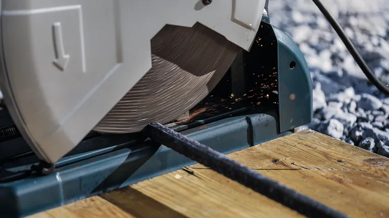 Cut-off saw slicing through a metal rod on a wooden platform.