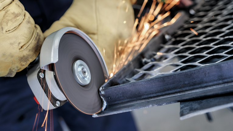 PRO Semi-Flexible Grinding Disc, 100 x 2 x 16 mm Person wearing safety equipment cuts metal mesh with a spinning angle grinder.