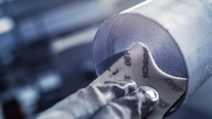 Person wearing safety equipment sands the inside of a metal pipe.