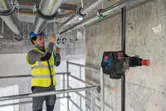 A person wearing safety equipment aligns pipes using a laser leveling tool.