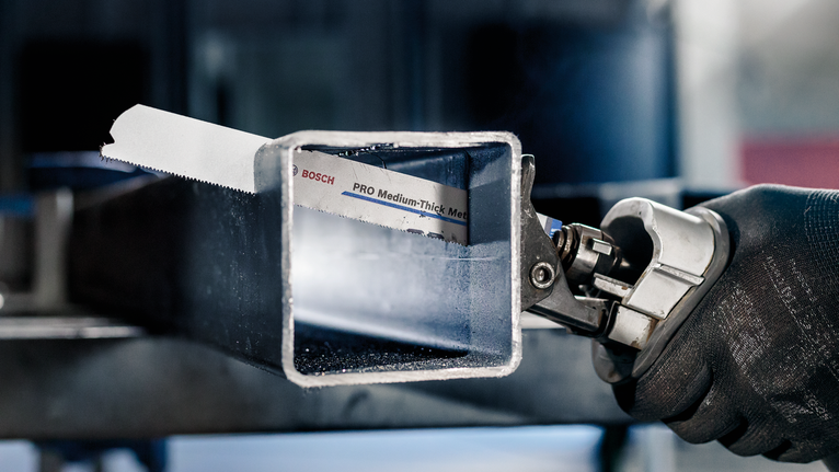 Person wearing safety equipment cuts a metal square tube with a power saw.