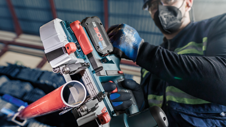 PRO CB2824 Band Saw Blade, 733 mm, 2 pcs A person wearing safety equipment uses a cordless power tool to cut a metal pipe.