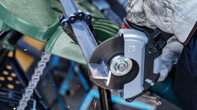 Person wearing safety equipment cuts metal pipe with a circular saw.
