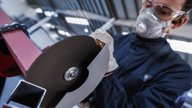 Person wearing safety equipment cuts metal with a spinning angle grinder.