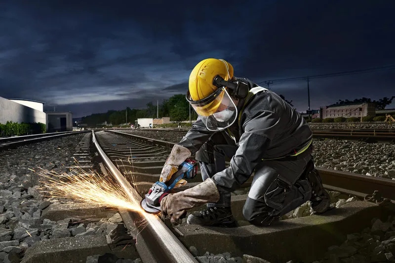GWS 18V-11 S A person wearing safety equipment uses an angle grinder to cut a railway track.